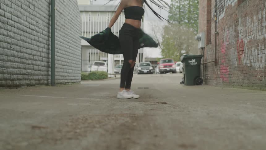 A woman spins around in a circle in a graffiti lined alley