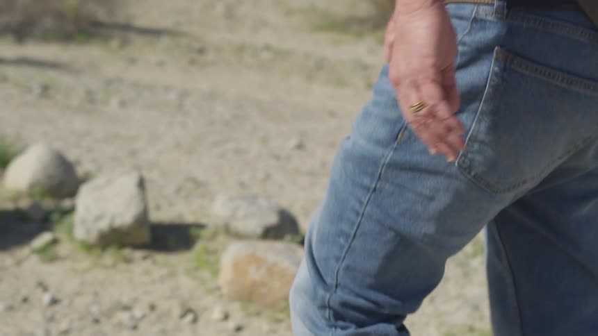 A man walks down a gravel path while wearing blue jeans a blue shirt and a fanny pack