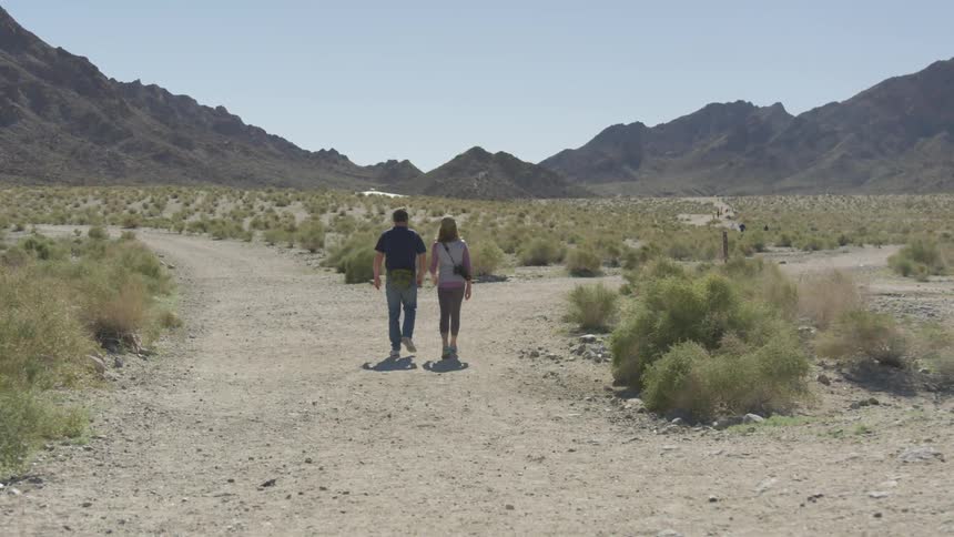 A man and a woman hike through a desertsurrounded by mountains