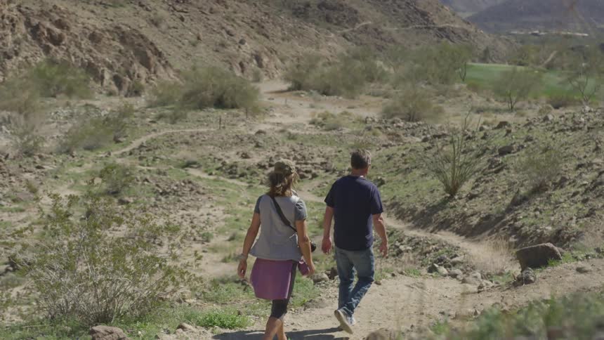 Man and woman walk on a rocky trail through the hills