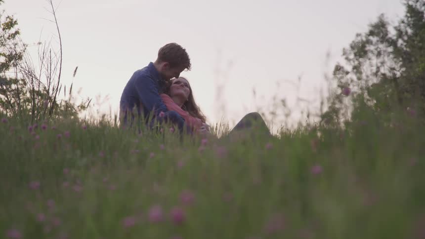 Man and woman sit in field outside cuddling
