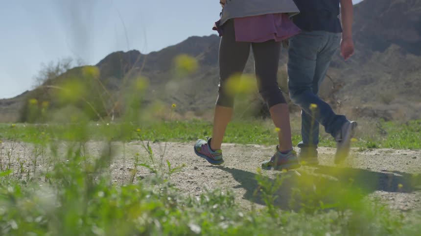 Male and female walk together along a dirt trail near a hill