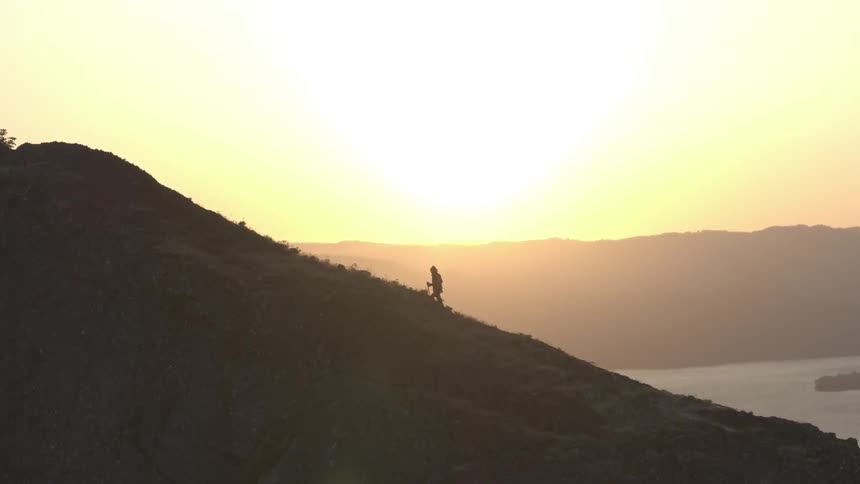 A hiker climbs up a mountainside near a lake at sunset