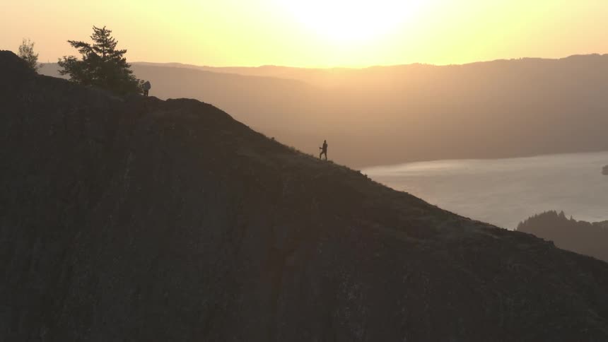 Two people standing on a cliff overlooking a lake