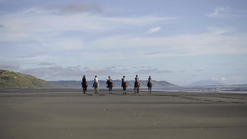 A group of six men ride horses across a sandy beach by the ocean. Great for visuals about travel.