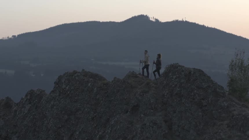 Couple standing on top of the edge of a mountain peak overlooking a lake