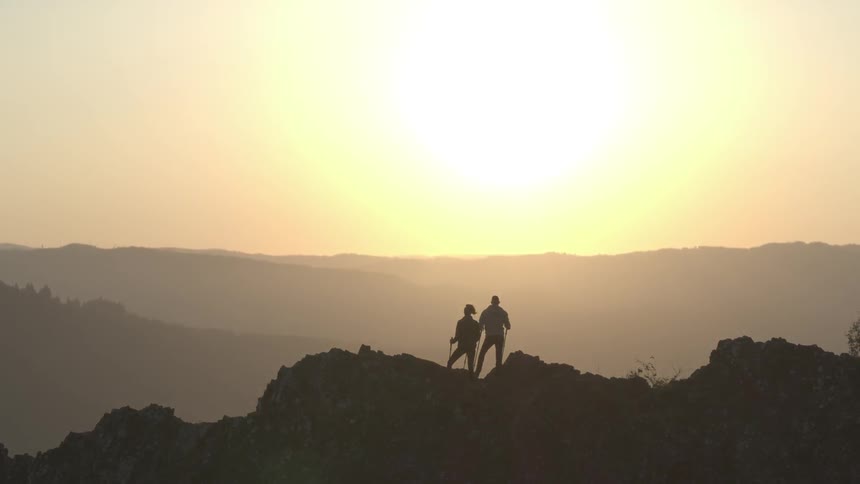 Two people stand on a peak overlooking a lake at sunrise