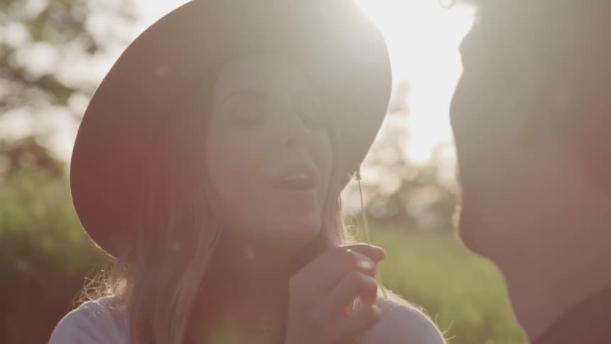 A woman outside in a grassy field blowing a dandelion in a mans face