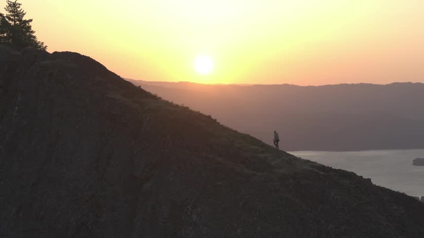 Aerial view of man hiking up a steep mountain at sunset