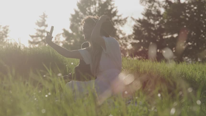 A man and woman sit in a field and take a selfie