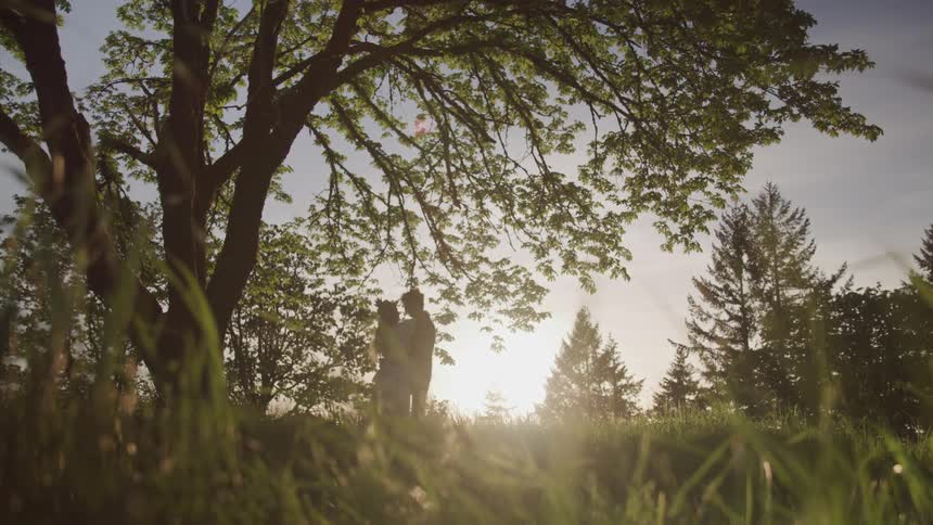 Man and woman walk on the grass and cuddle while the sun goes down