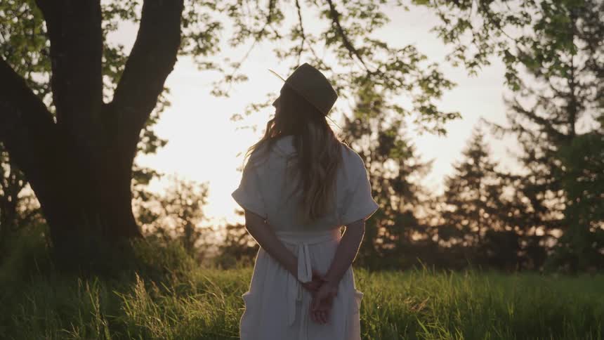 A woman wearing a sun hat looks toward the trees and horizon