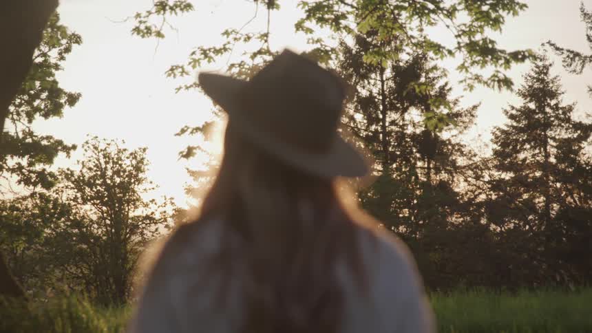 A woman wearing a hat stands underneath a tree and looks to the horizon