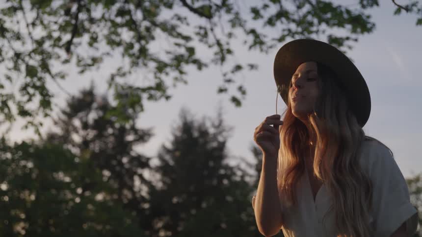 Woman blows a dandelion flower and scatters the seeds