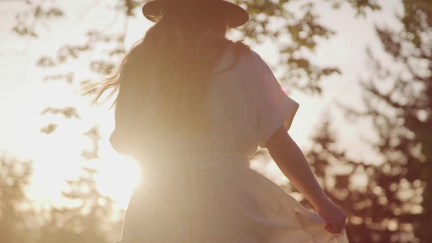 A woman with sun hat walking towards the sunset at the park