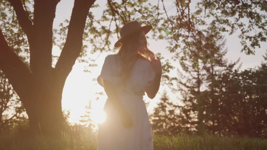 A woman is outdoors wearing a hat and dress