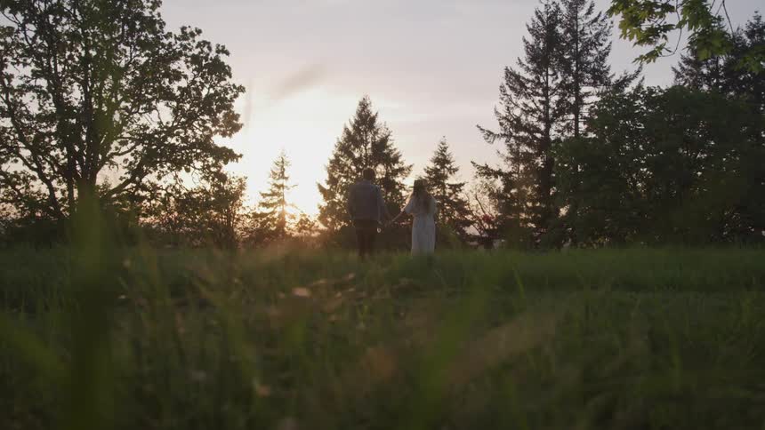 Man and woman walk through field hand in hand