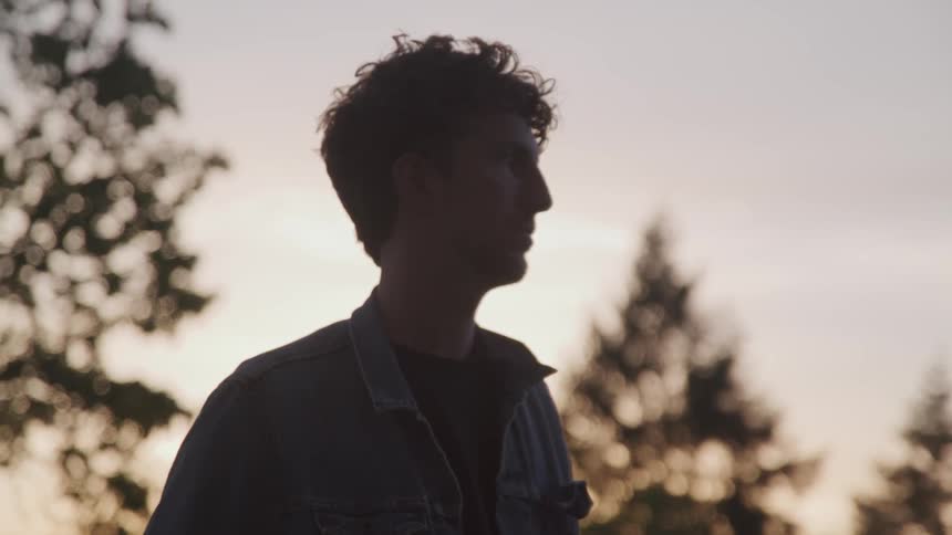 Man stands and looks ahead in the forest at dusk