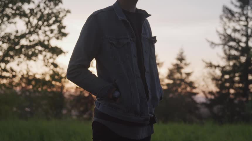 A young man stands alone in a grassy field at dusk