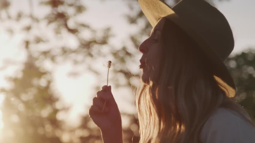 A woman blows a dead dandelion