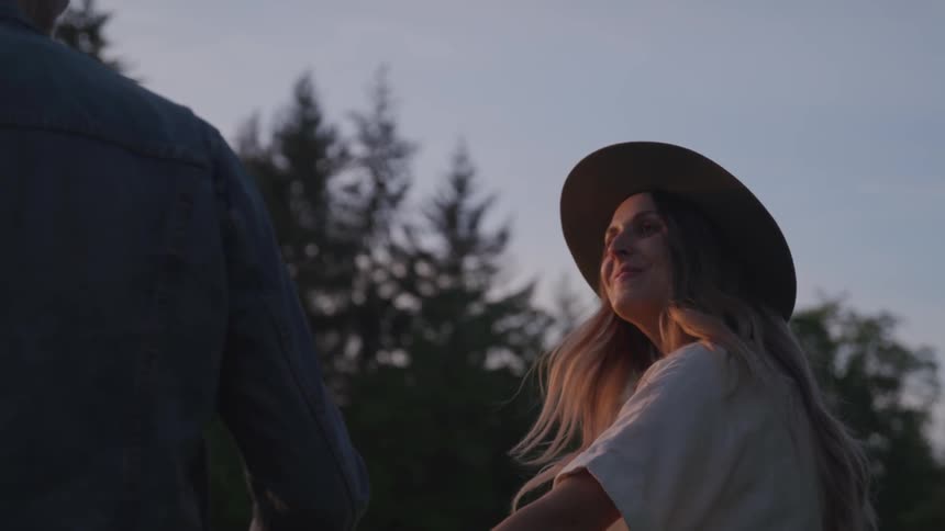 Man and woman hold hands in the forest at sunset