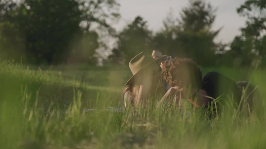 A man and woman kiss and flirt while lying in a grassy field