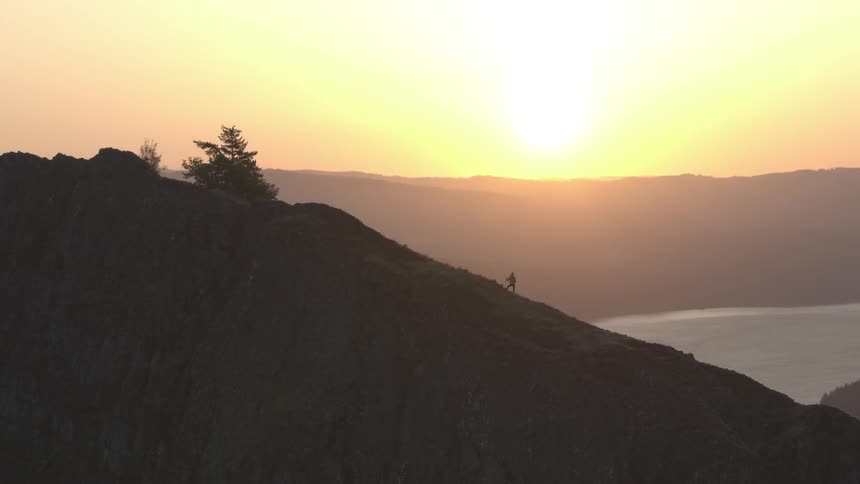 Camera is orbiting a person standing on a mountain slope far away