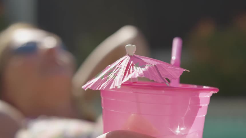 A woman laying in a pool holding a pink cup with a pink umbrella and a pink straw