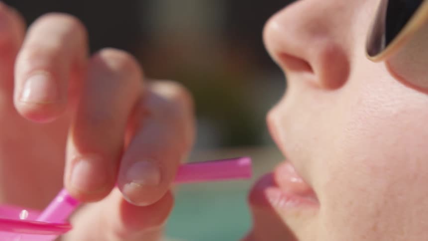 A woman picks up a cup and drinks out of a pink straw