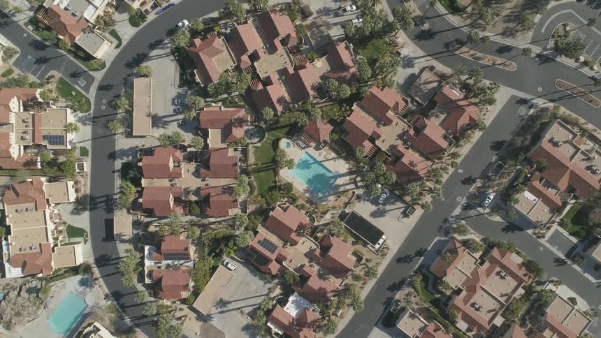 Rooftops of homes surrounding swimming become more distant as aerial view reveals streets and layout of a neighborhood community