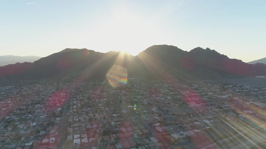 An aerial scenery of a city landscape with a mountain and a sun flare behind it