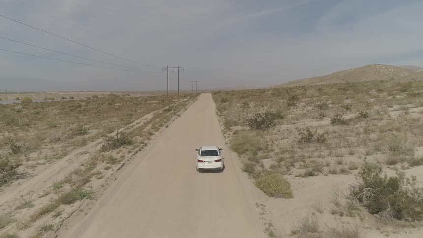 A white car travels on a dirt desert road