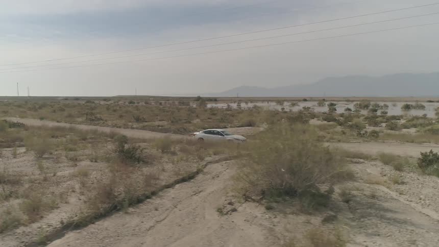 White car goes down on the dirt road on a sunny day