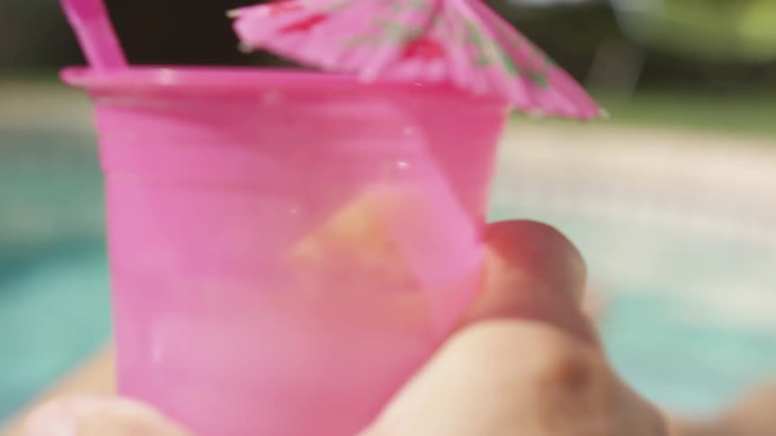 A woman lifts a pink plastic cup with a cocktail umbrella to drink from it