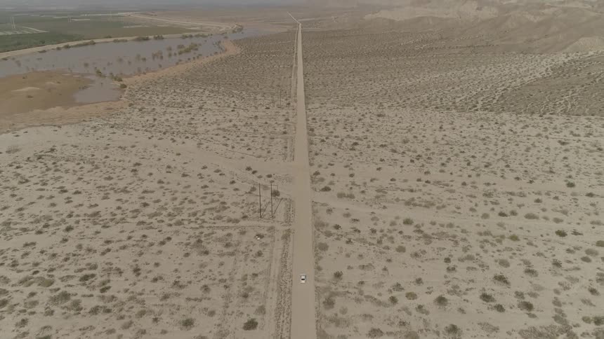 A vehicle drives down a deserted desert dirt road