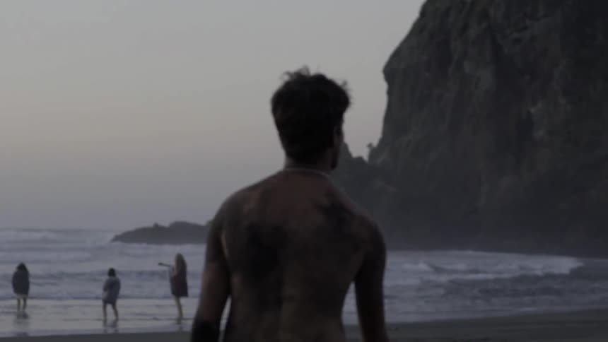 A man strolls along the shoreline at sunset, with warm light reflecting off the water.