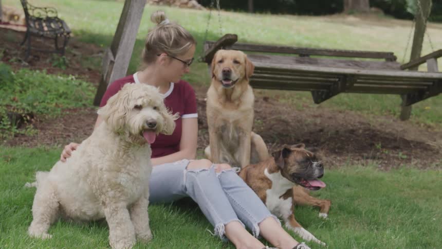 A woman sits with three dogs in the yard