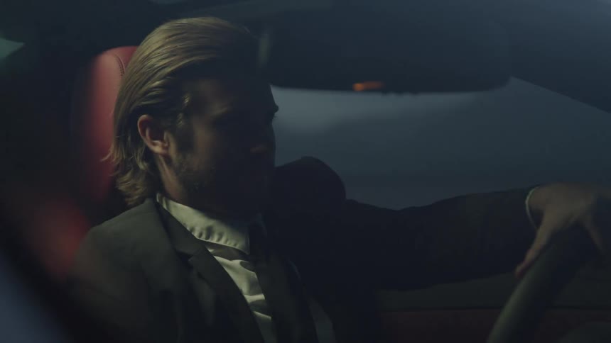 Blonde man in black suit drives a sport car at night