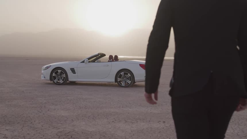 A person walks towards a car parked on a dry lake bed