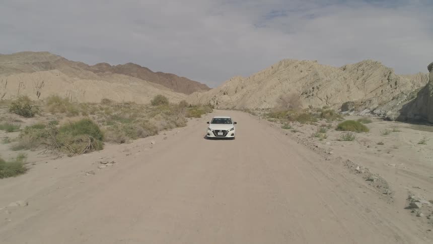 A white car drives down a dirt road in the desert