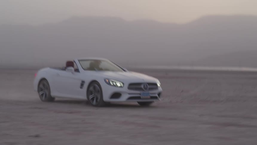 A white car is driving quickly through a barren desert