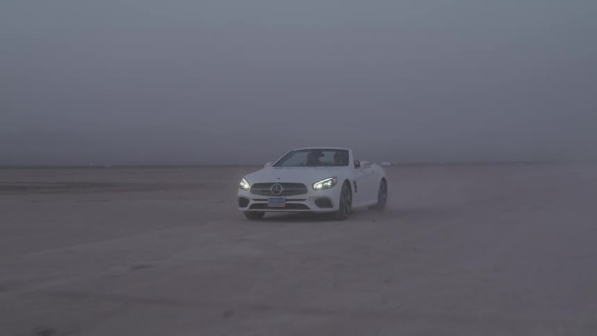 A white sports car with headlights on is speeding across salt flats