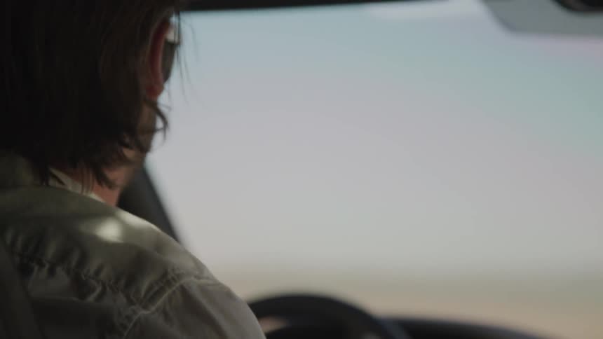 Man in sunglasses with scruffy beard driving car