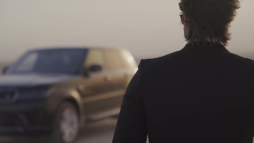 A man in a suit looks toward a vehicle