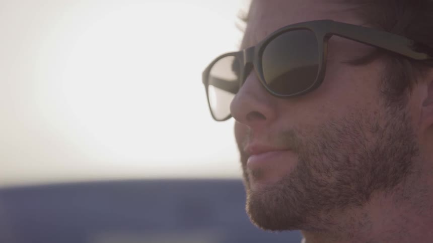 Bearded man wearing sunglasses gazes ahead as his hair blows in the wind