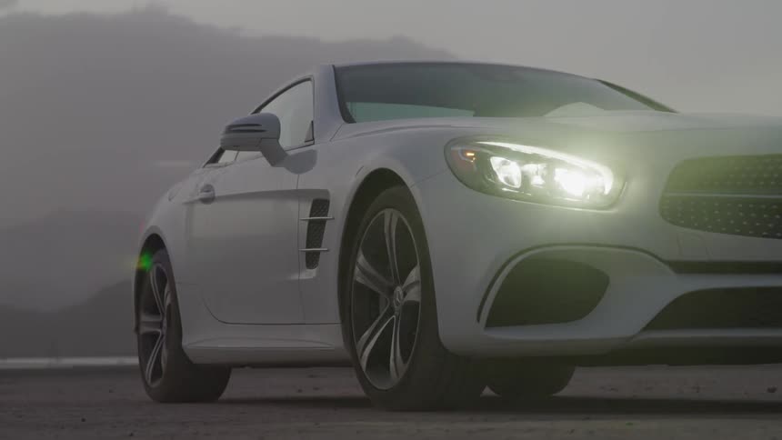 White sports car parked in desert with the lights on with mountain in the background