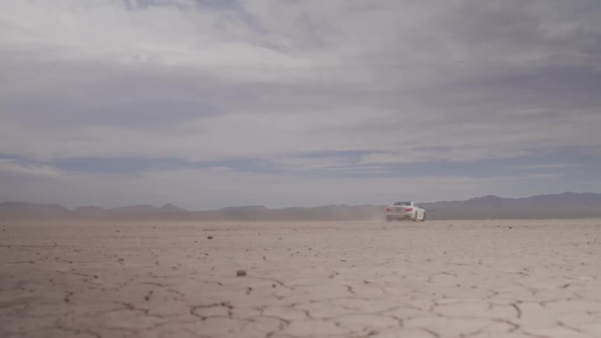 White car speeding on an open dirt road in the desert