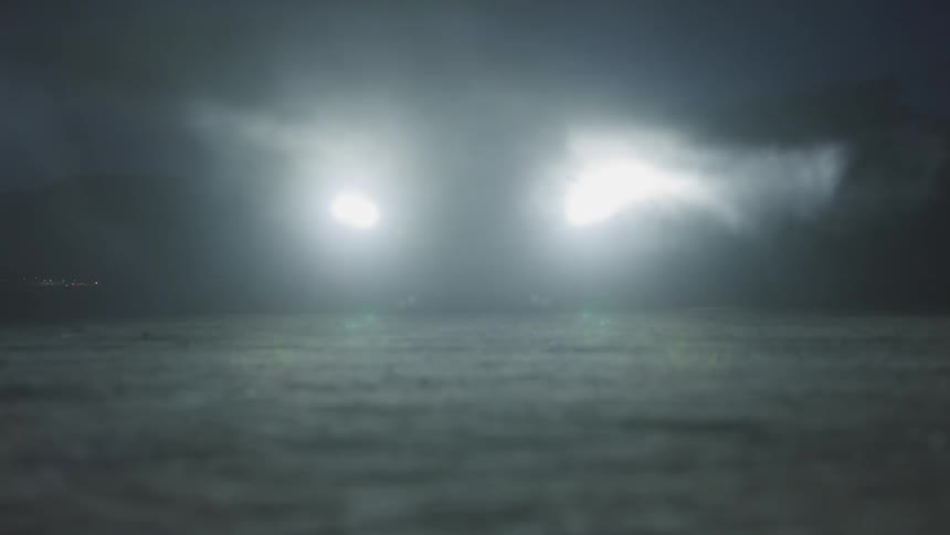 In the darkness of night an headlights from an automobile shine brightly through a swiftly blown fog