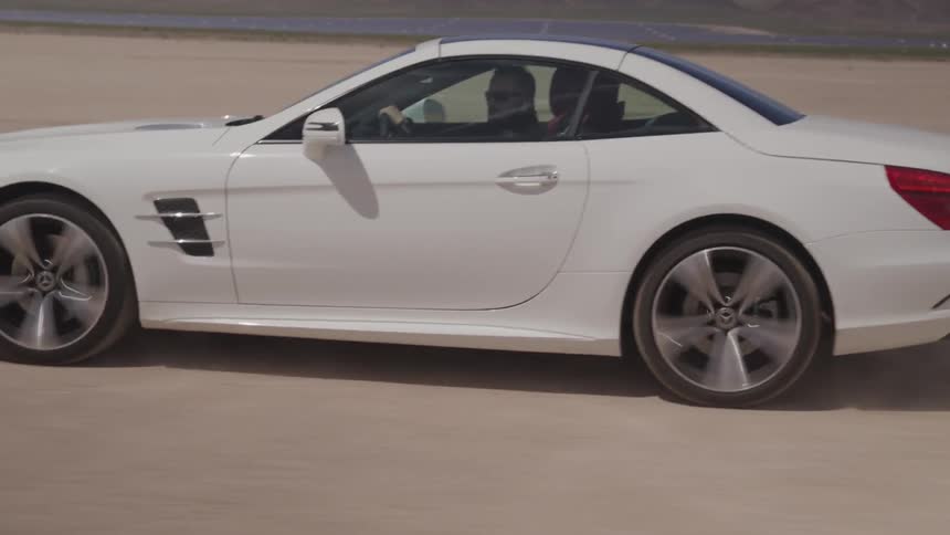 A man drives a white car over a desert floor