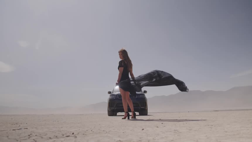 A woman in heels stands in front of a black range rover parked on the salt flats